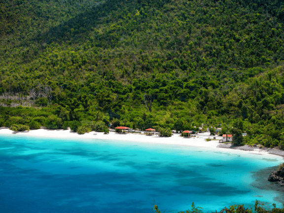 White beach and turquoise water in Maho Bay, US Virgin Island, with a green forest in the back.